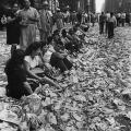 La gente si siede sul marciapiede tra i coriandoli del corteo che celebra la fine della seconda guerra mondiale. 14 ago 1945