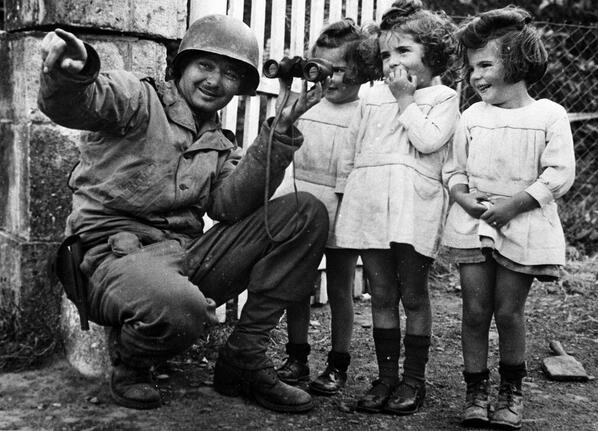Tre bambine scrutano attraverso il binocolo di un soldato americano dopo la liberazione della Normandia 1944