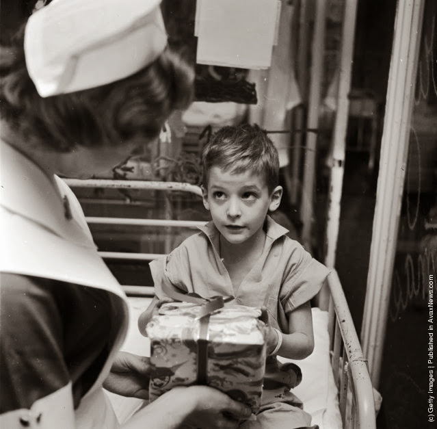 Un giovane paziente del reparto pediatrico del Lenox Hill Hospital, in America, riceve un inaspettato regalo di Natale dall'infermiera Linda Gross. (Photo by Vecchio: Three Lions: Getty Images). circa 1955