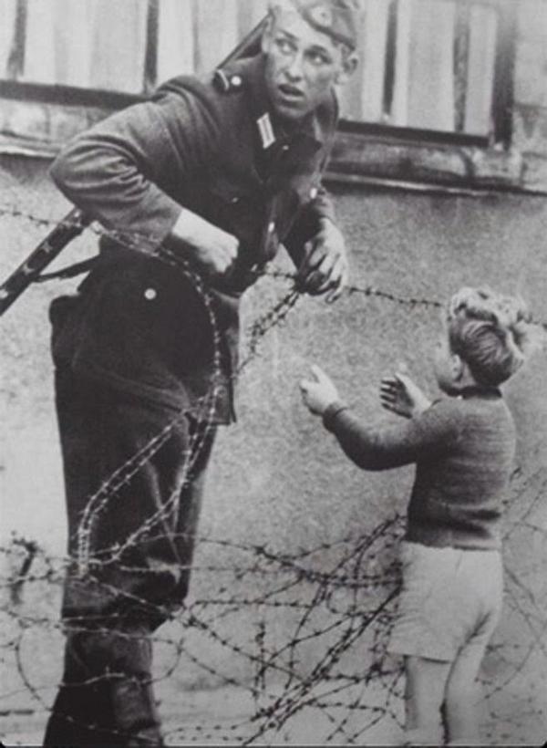 Un soldato tedesco dell'est aiuta un bambino a scavalcare il neonato Muro di Berlino, 1961