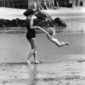 Una madre gioca con il suo bambino sulla spiaggia. [C. 1950]