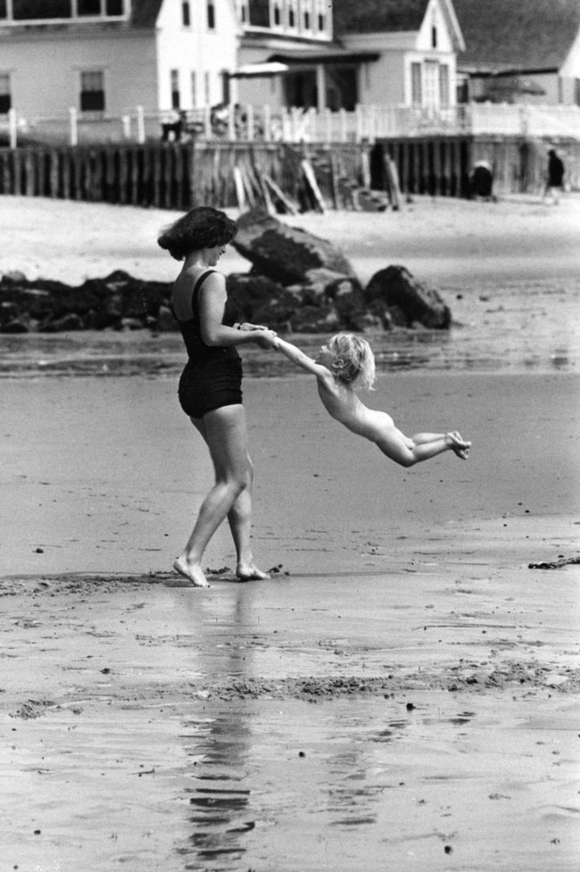 Una madre gioca con il suo bambino sulla spiaggia. [C. 1950]