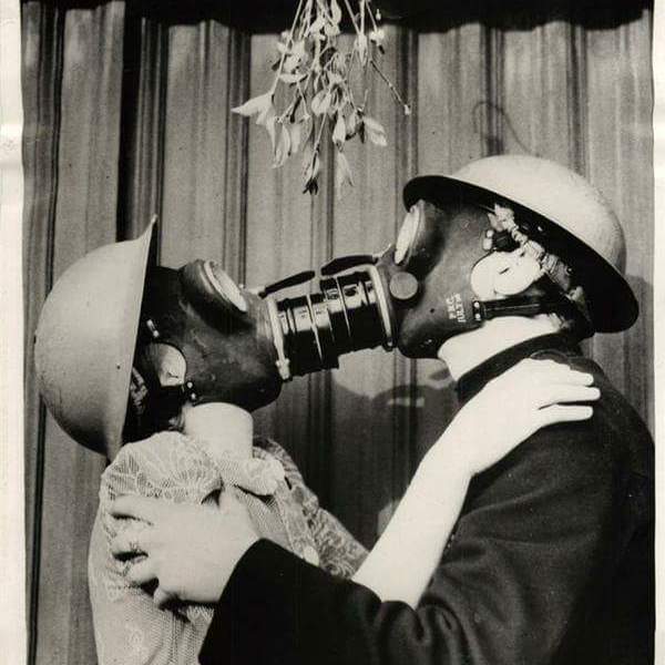 Coppia con maschere antigas si bacia sotto il vischio. Seconda guerra mondiale