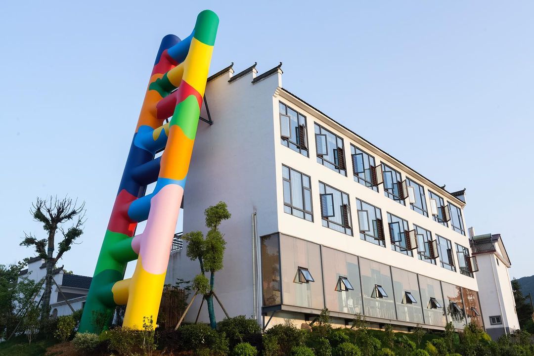 Italian artist Paola Pivi ascends at FULIANG 2021 with a monumental installation entitled Untitled (ladder). The installation consists of a graphic inflatable staircase over 20 meters tall propped against a banal two-story building.
